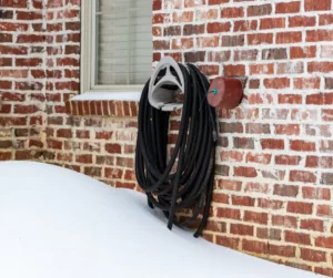 A garden hose wrapped on a holder against a brick wall, partially buried by snow in winter.